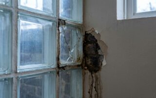 Rissiger Glasbaustein mit feuchtem Rand und abplatzendem Putz am Wandanschluss